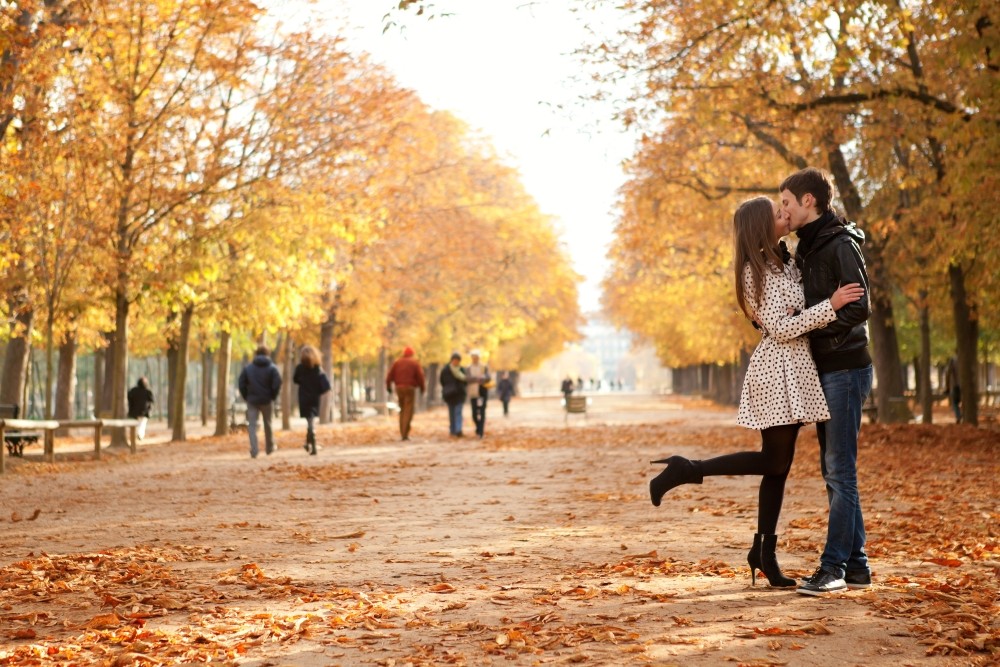 young couple kissing surrounded by falling autumn leaves