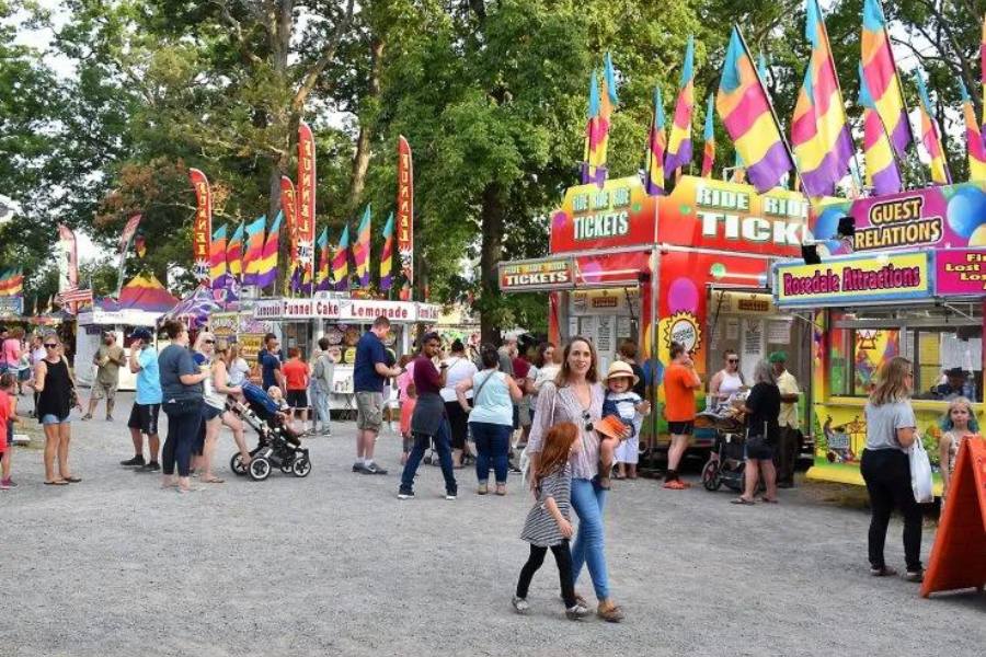 Woman walking with her children past a row of stands at a county fair