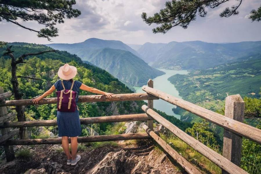 Girl on a hiking trail looking over a valley with mountains and a river
