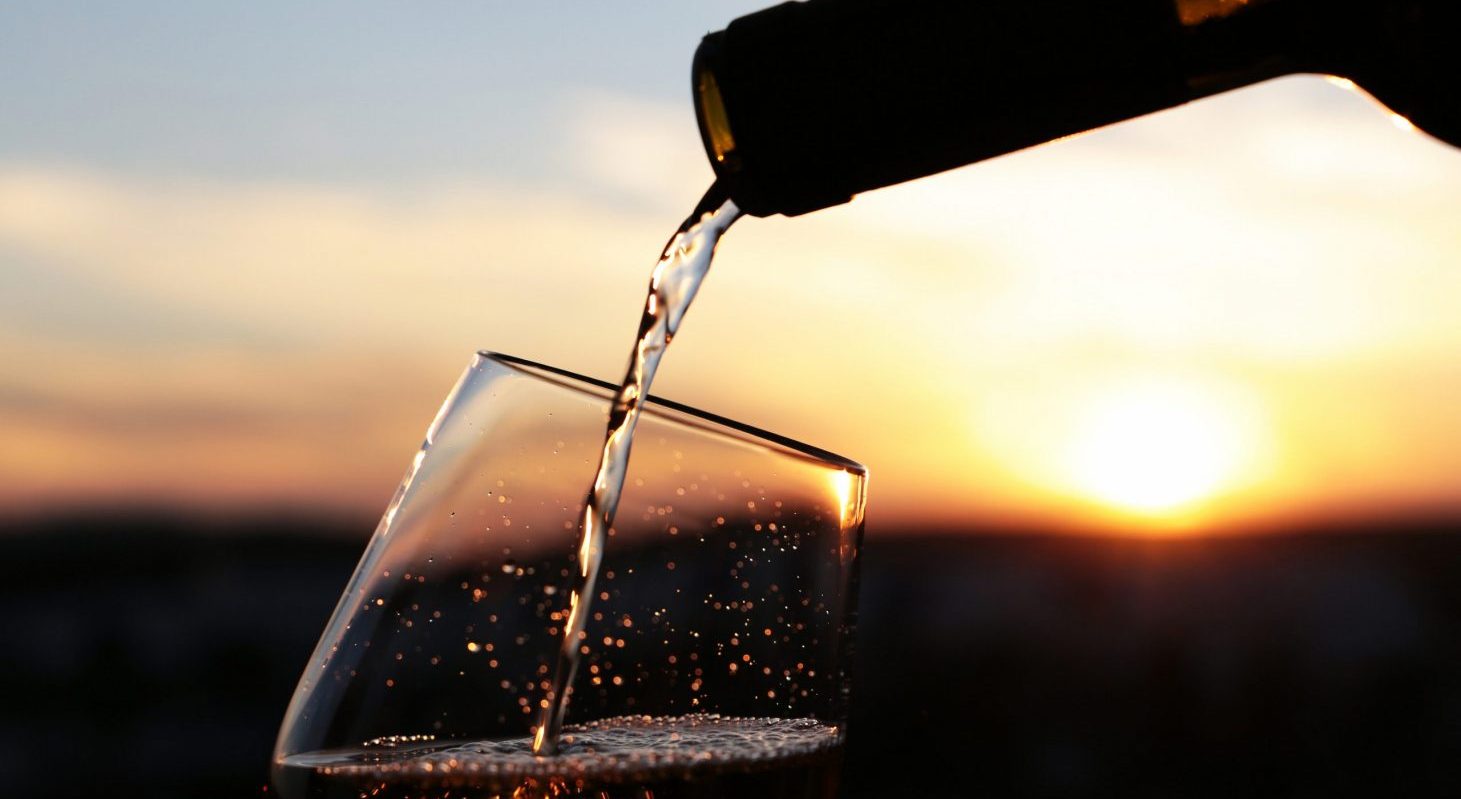 A glass of white wine being poured with a sunset in the background